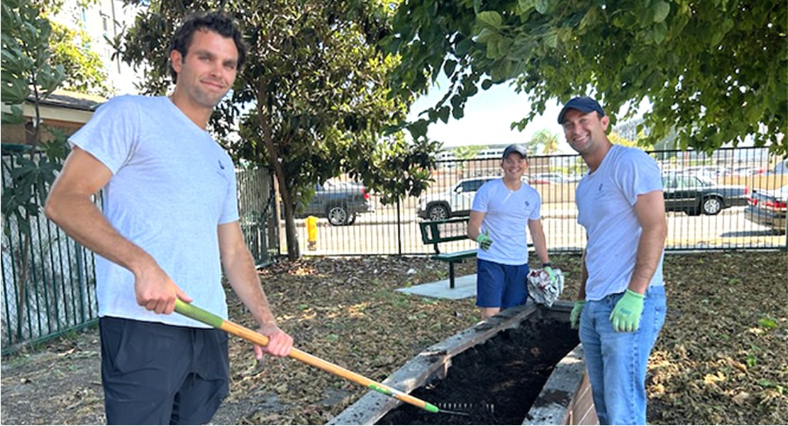 Three employees helping to plant a garden while raking a flower bed.