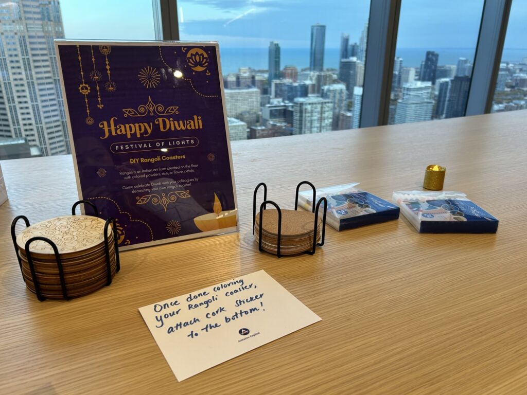A photo of a sign that says "Happy Diwali - Festival of Lights" on a desk. There are skyscrapers in the background outside the windows.