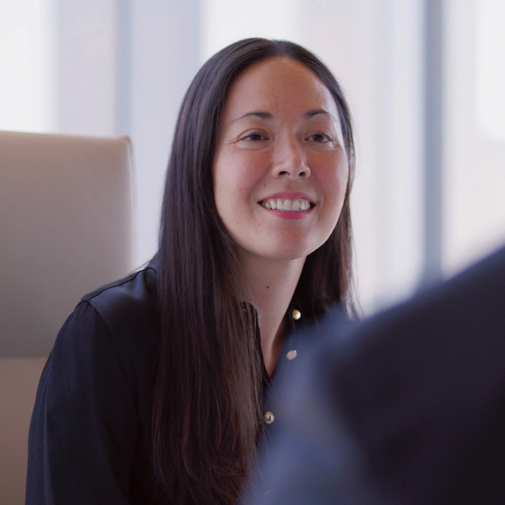A feminine subject in business attire, smiling while looking at another figure.