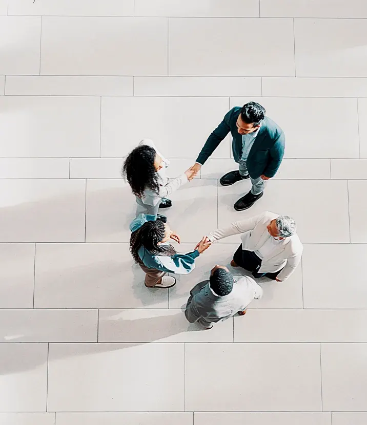 An overhead view of five people in business formal clothing. Two sets of people are shaking hands.