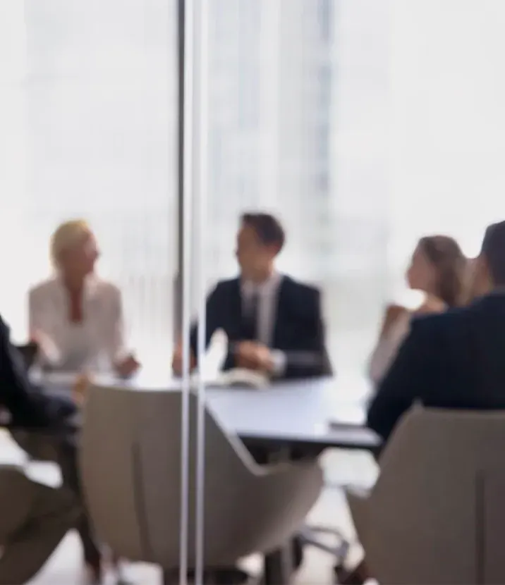 An out-of-focus photo of people at a meeting desk.